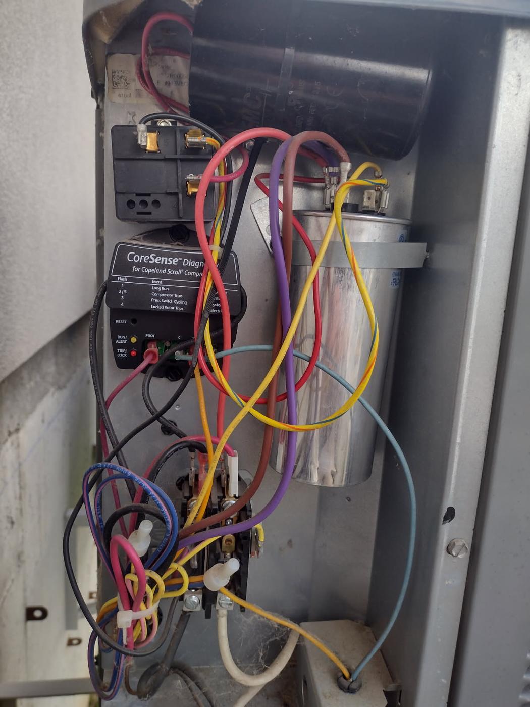 The opened electrical panel of a condensing unit, showing the contactor, run capacitor and a compressor diagnostic module